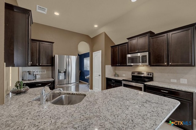 kitchen with stainless steel appliances, sink, light stone counters, and dark brown cabinetry