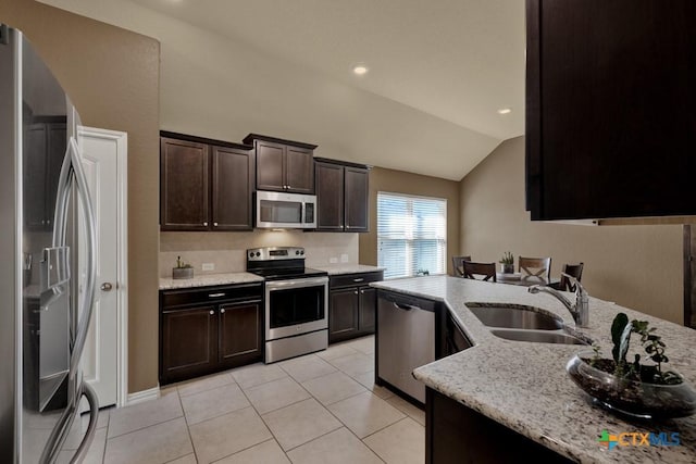 kitchen with vaulted ceiling, appliances with stainless steel finishes, sink, light stone countertops, and dark brown cabinets