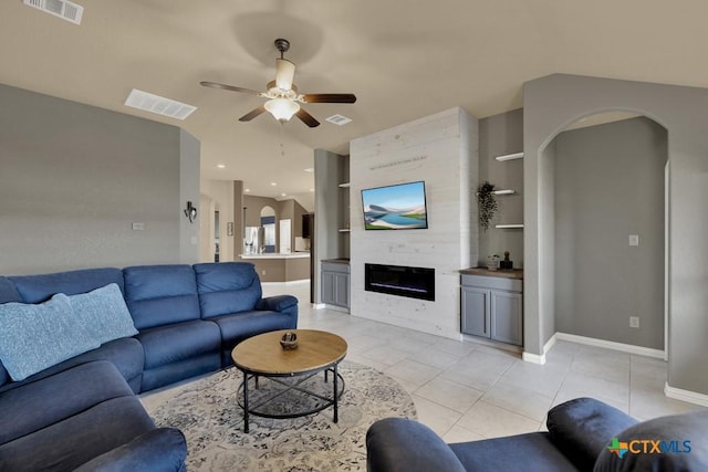 tiled living room featuring built in shelves, a large fireplace, and ceiling fan