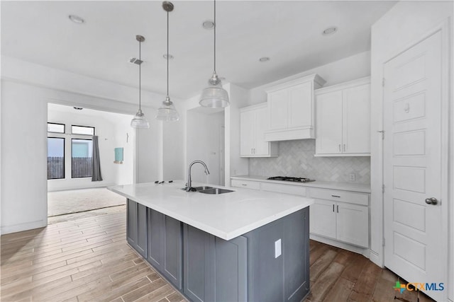 kitchen with a sink, gas cooktop, tasteful backsplash, wood finished floors, and white cabinets