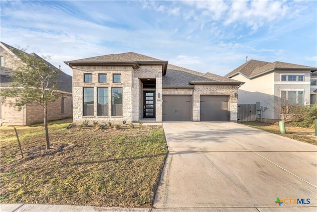 prairie-style home with brick siding, an attached garage, fence, roof with shingles, and driveway