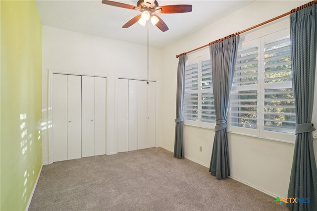 unfurnished bedroom with ceiling fan, light colored carpet, and two closets