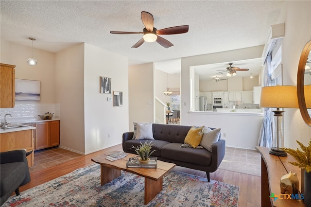 living room with a textured ceiling, light wood-type flooring, ceiling fan, and sink