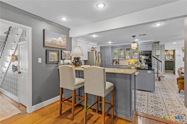 kitchen with a breakfast bar, stainless steel fridge, gray cabinets, ornamental molding, and kitchen peninsula