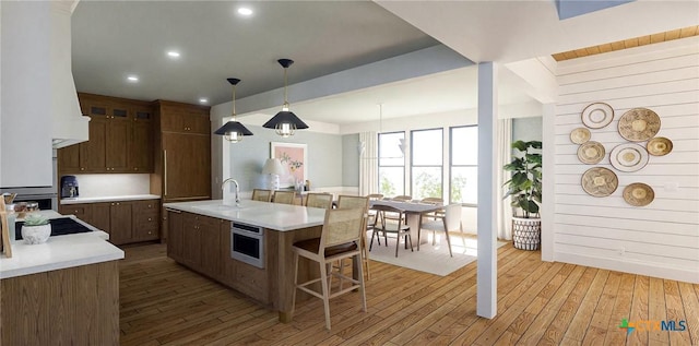 kitchen featuring sink, wall oven, pendant lighting, a center island with sink, and hardwood / wood-style flooring