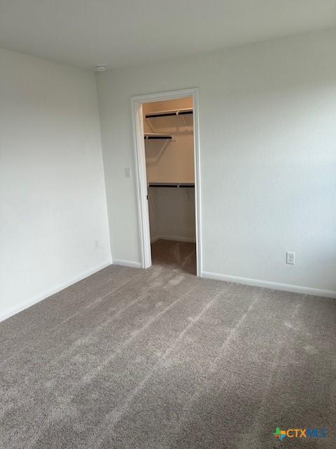 unfurnished bedroom featuring a walk in closet, baseboards, carpet, and a closet