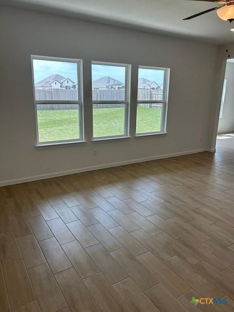 empty room with baseboards, plenty of natural light, wood finished floors, and a ceiling fan