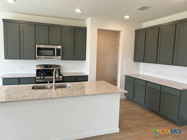kitchen featuring light stone countertops, visible vents, a sink, stainless steel microwave, and range