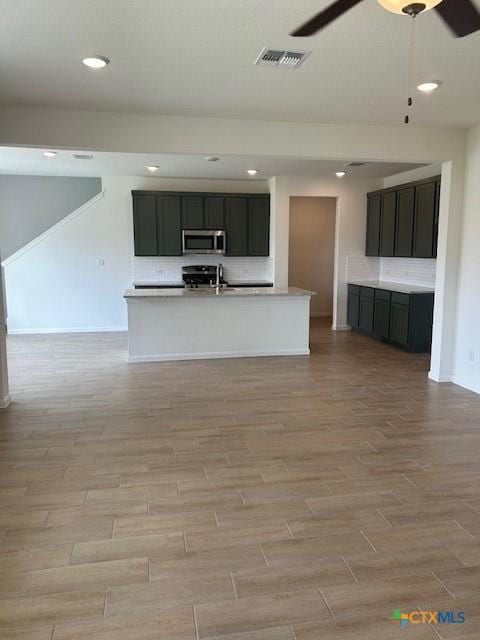 kitchen featuring light wood finished floors, stainless steel microwave, visible vents, light countertops, and a ceiling fan
