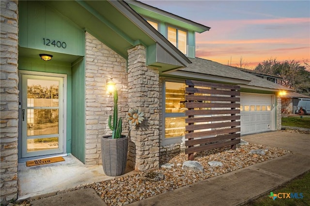 property entrance with a garage, stone siding, roof with shingles, and driveway