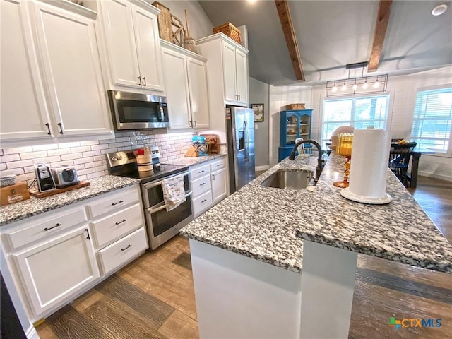 kitchen with sink, beamed ceiling, appliances with stainless steel finishes, white cabinets, and hardwood / wood-style flooring