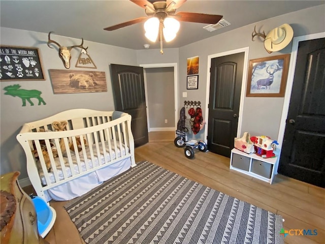 bedroom featuring ceiling fan, a crib, and hardwood / wood-style flooring