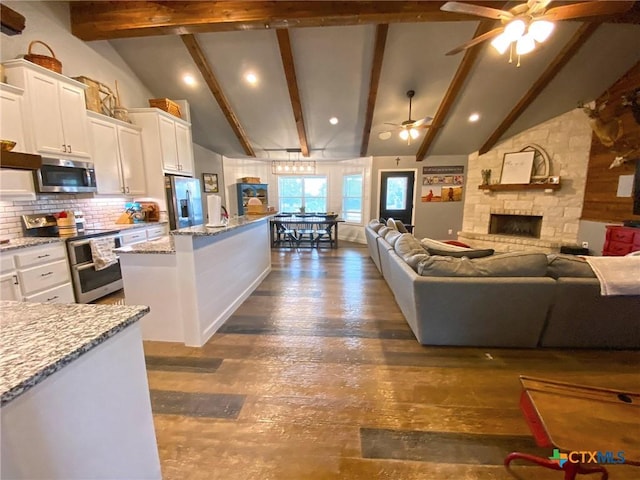 kitchen with vaulted ceiling with beams, stainless steel appliances, open floor plan, light stone countertops, and dark wood-style floors