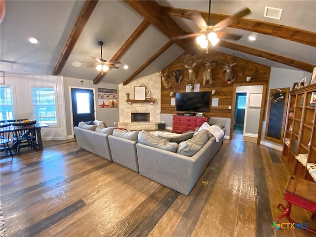 living room with a stone fireplace, ceiling fan, dark wood-type flooring, and lofted ceiling with beams