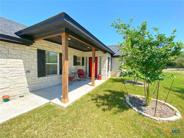 rear view of property with a shingled roof, stone siding, a patio area, and a lawn