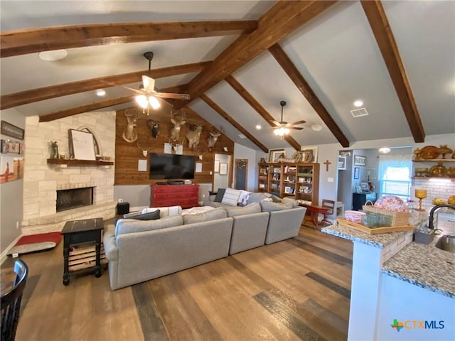 living room with lofted ceiling with beams, sink, ceiling fan, a fireplace, and wood-type flooring