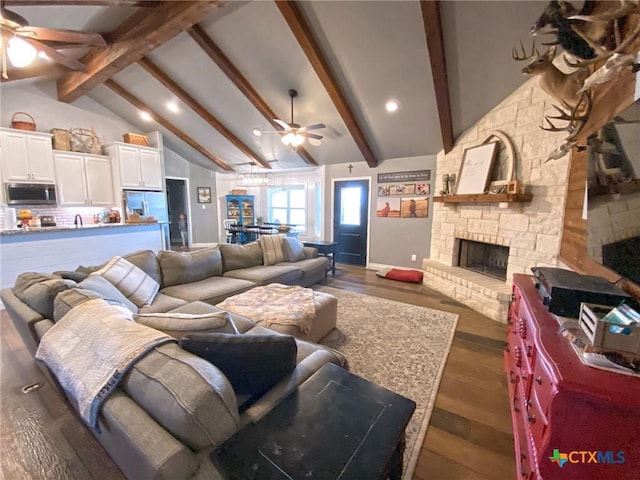 living room featuring a ceiling fan, a stone fireplace, lofted ceiling with beams, and wood finished floors