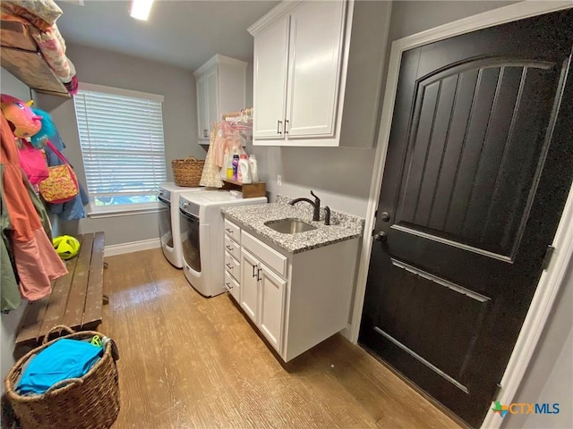 laundry room with washing machine and clothes dryer, light hardwood / wood-style flooring, cabinets, and sink