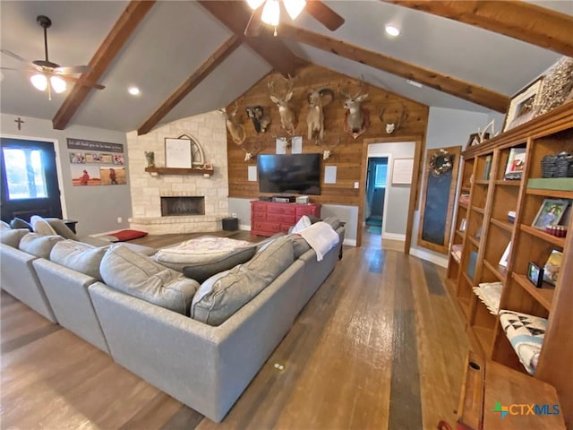 living room with vaulted ceiling with beams, ceiling fan, wood finished floors, and a stone fireplace