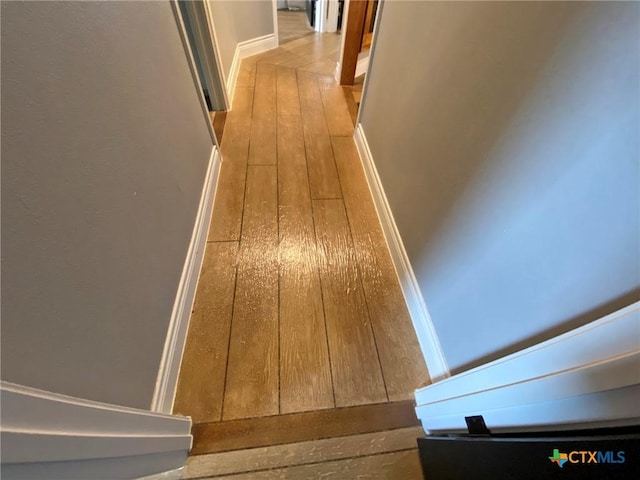 hall featuring wood-type flooring and baseboards