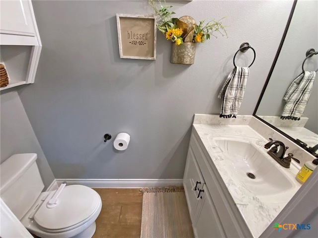 half bathroom with baseboards, vanity, and toilet