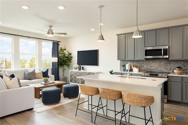 kitchen featuring stainless steel appliances, sink, an island with sink, gray cabinetry, and light wood-type flooring