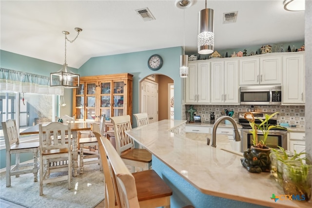 kitchen with stainless steel appliances, hanging light fixtures, white cabinets, and a kitchen bar