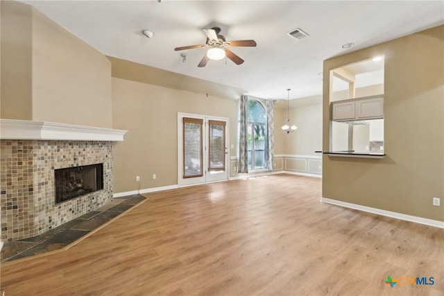 unfurnished living room with hardwood / wood-style floors, ceiling fan with notable chandelier, and a tile fireplace