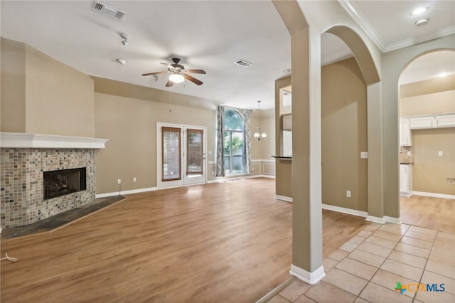 unfurnished living room with light wood-type flooring, ceiling fan with notable chandelier, crown molding, and a fireplace