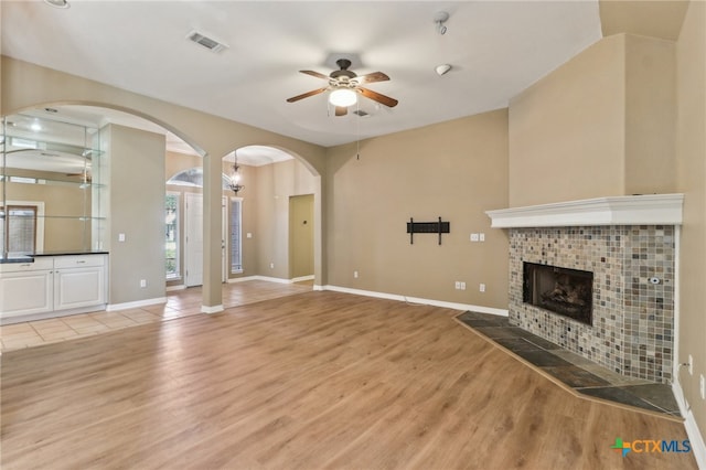 unfurnished living room with wood-type flooring, ceiling fan, and a tile fireplace