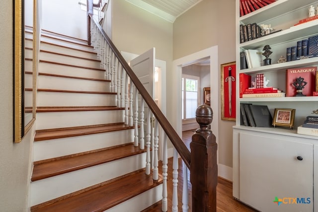 stairway with ornamental molding and wood-type flooring