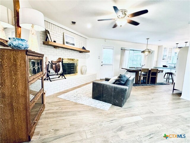 living room featuring ceiling fan, light hardwood / wood-style floors, and a brick fireplace