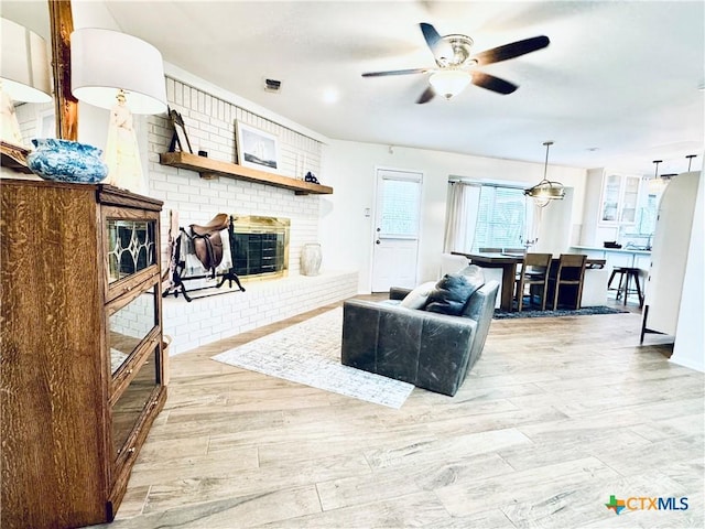 living area with a ceiling fan, light wood-style flooring, a fireplace, and visible vents