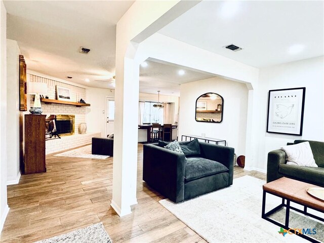 living area featuring visible vents, light wood-style flooring, a brick fireplace, and baseboards