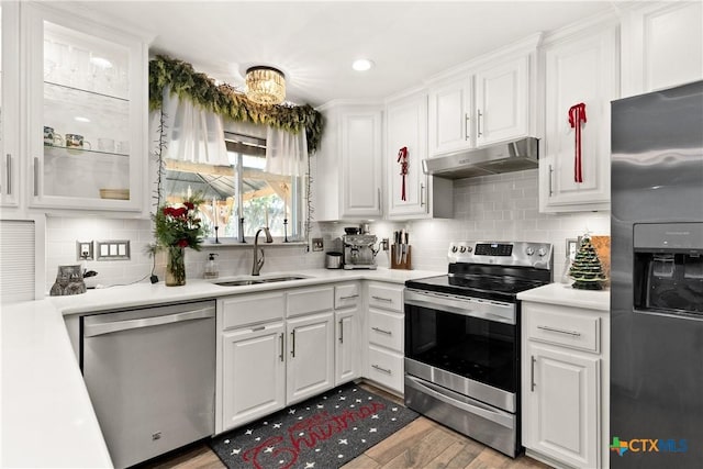 kitchen with sink, backsplash, light hardwood / wood-style floors, white cabinets, and appliances with stainless steel finishes