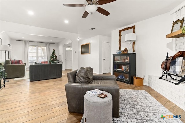 living room featuring ceiling fan, light wood-type flooring, and a fireplace