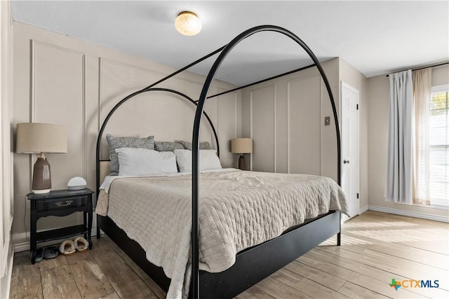 bedroom with a decorative wall, baseboards, and wood finished floors