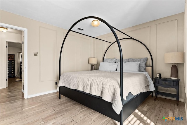 bedroom featuring a decorative wall, baseboards, visible vents, and wood finished floors