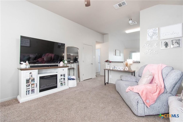 carpeted living area featuring lofted ceiling, visible vents, a glass covered fireplace, ceiling fan, and baseboards