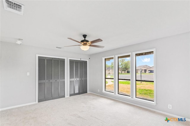 unfurnished bedroom featuring multiple closets, visible vents, carpet flooring, a ceiling fan, and baseboards