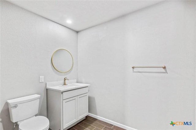 bathroom with vanity, wood finish floors, baseboards, and toilet