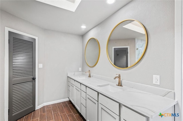 bathroom with a sink, double vanity, wood finish floors, and baseboards