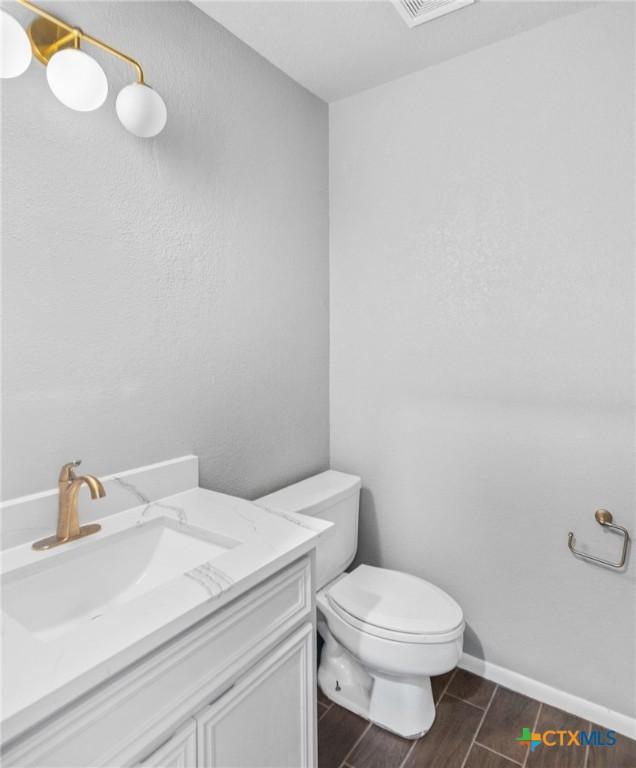half bath featuring vanity, toilet, baseboards, and wood finish floors