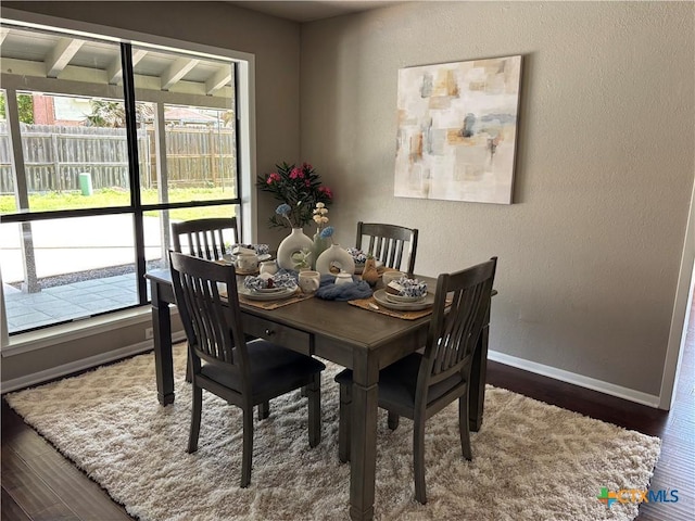 dining space with beam ceiling, a textured wall, baseboards, and wood finished floors