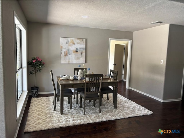 dining space with baseboards, visible vents, a textured ceiling, and dark wood-type flooring