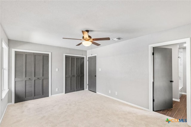 unfurnished bedroom with multiple closets, visible vents, ceiling fan, carpet flooring, and baseboards