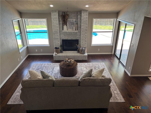 living room with wood finished floors, a fireplace, a textured ceiling, baseboards, and recessed lighting