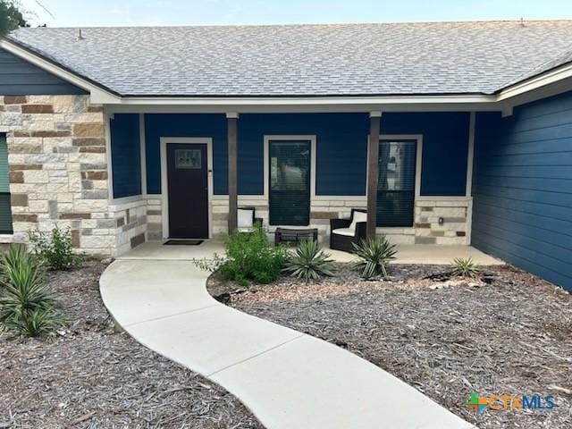 doorway to property featuring a porch, stone siding, and a shingled roof