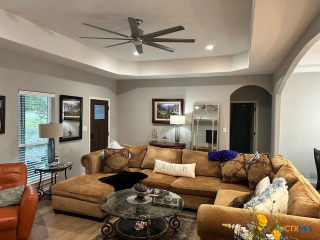 living area featuring arched walkways, a ceiling fan, a raised ceiling, wood finished floors, and recessed lighting