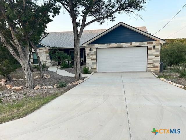 single story home featuring driveway, an attached garage, and stone siding